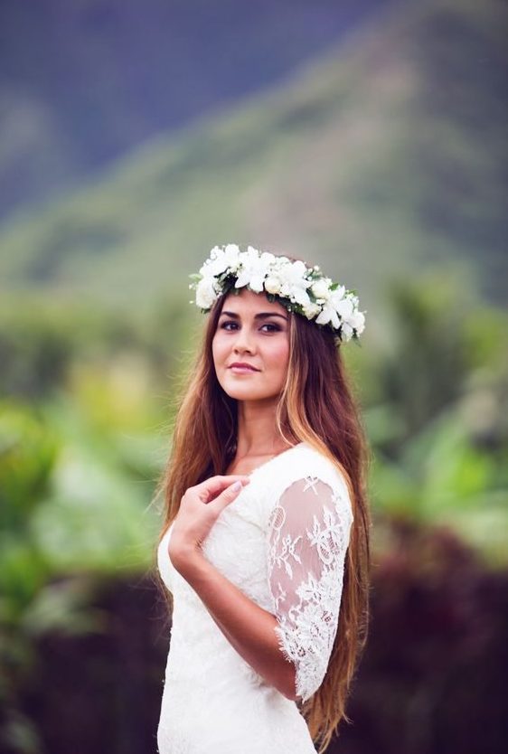 a beautiful bride looks at the camera wearing a flower crown full of white flowers and the jungle mountains behind her in the distance