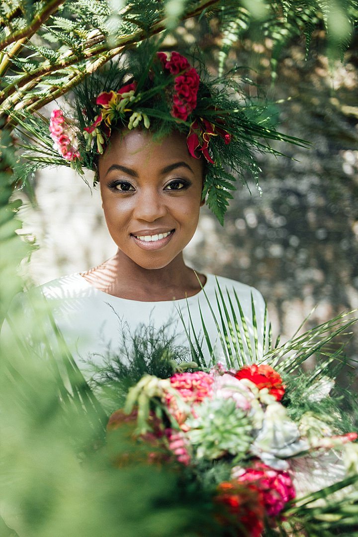 a beautiful bride looks at the camera and smiles while wearing a flower crown and holding her bouquet