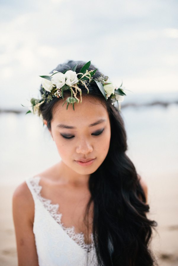 a bride looks thoughtful as she stands at the beach while wearing a flower crown