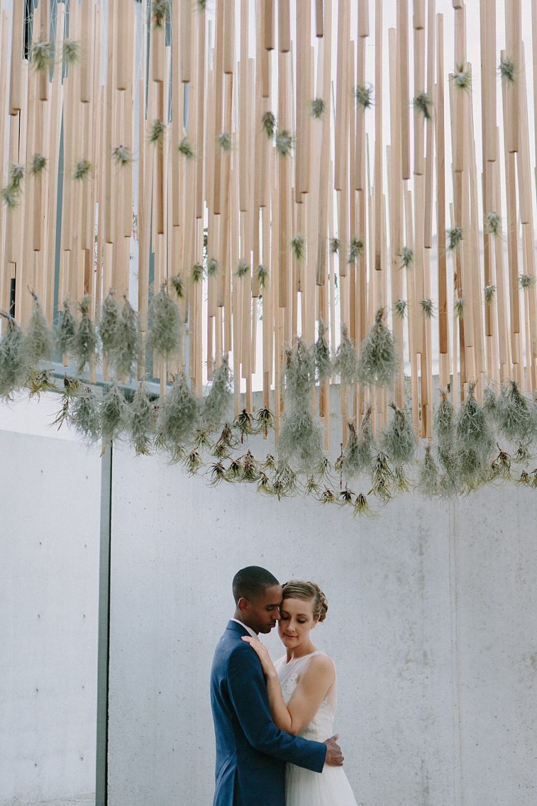 Bride and groom portrait in front of wood, air plants, and concrete