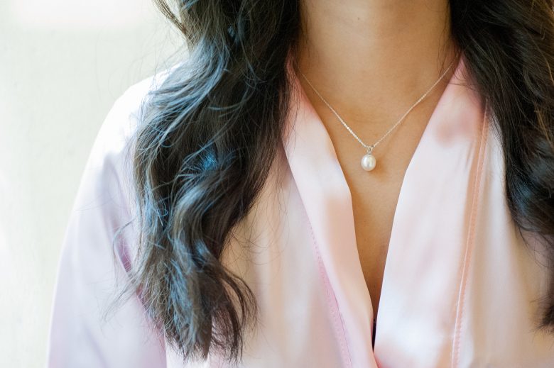 Close up of woman's neck and torso, wearing a pink robe and necklace with pearl