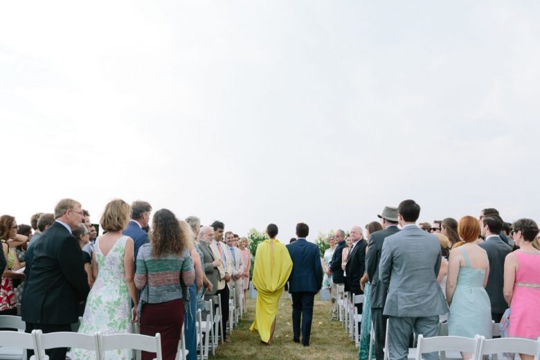 man and woman in yellow dress walking down aisle at wedding (photo from behind)
