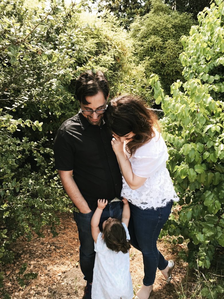 author and her husband looking down at a toddler in front of greenery