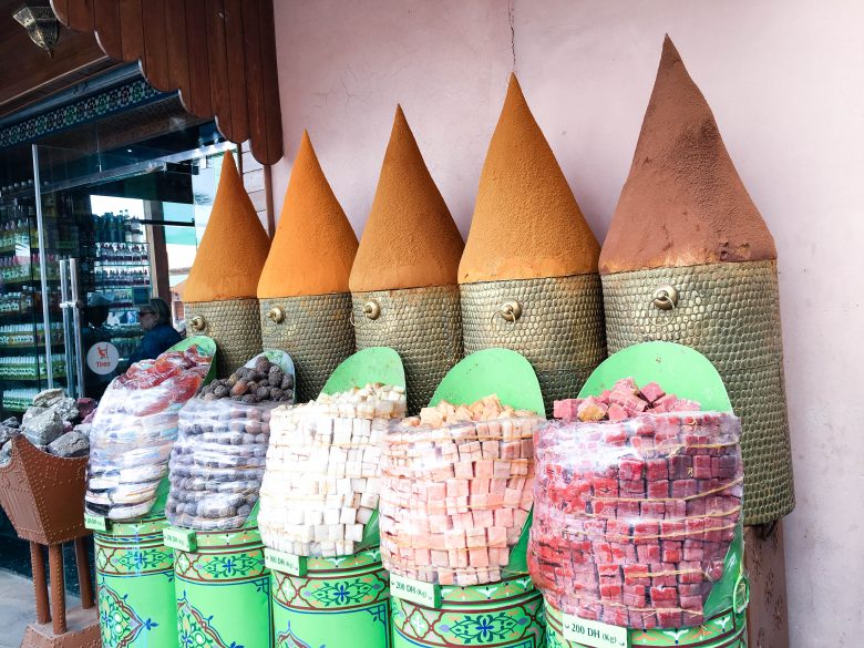 Moroccan treats in green ornate tins and piles of orange spices in baskets