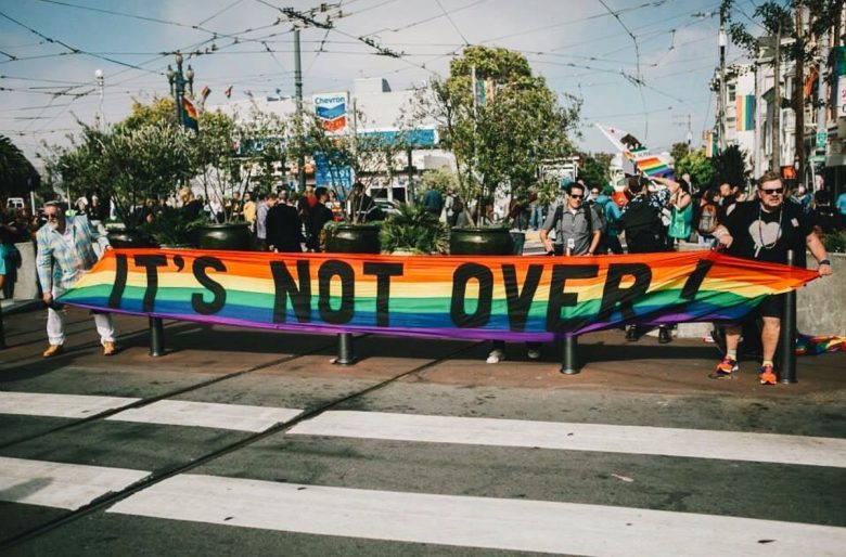 People holding a rainbow banner that reads "IT'S NOT OVER!" in the Castro in San Francisco