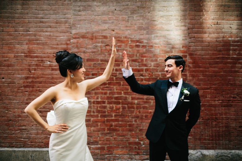 bride and groom high-fiving in front of red brick wall