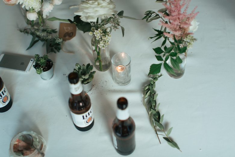 empty beer bottles on table with flowers in vases and succulents and a candle