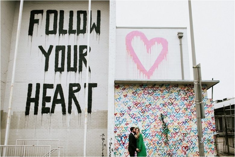 Bride and groom in front of heart-graffiti wall; "follow your heart" graffiti