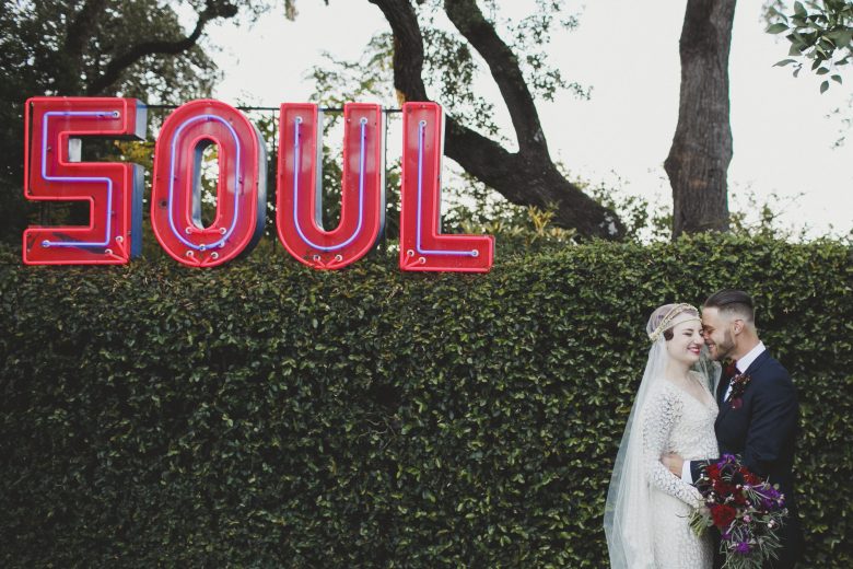 Bride and groom in front of hedge and neon "Soul" sign