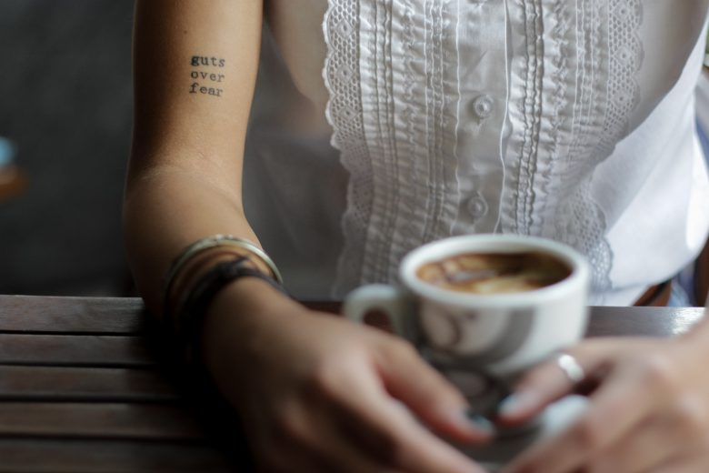 woman with coffee and "guts over fear" tattoo