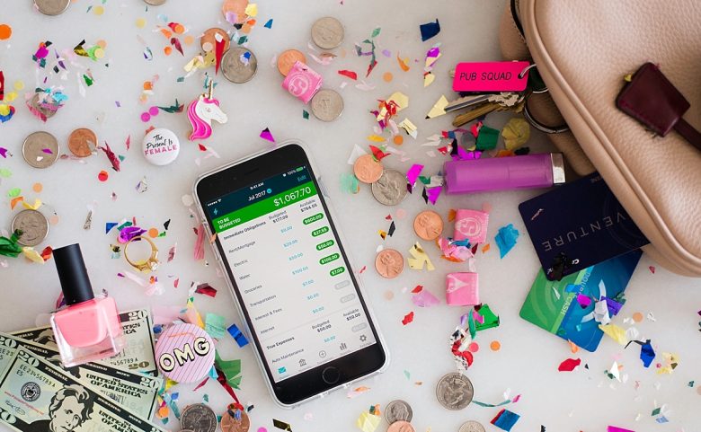 YNAB budget app on a cell phone surrounded by money and items from a woman's purse