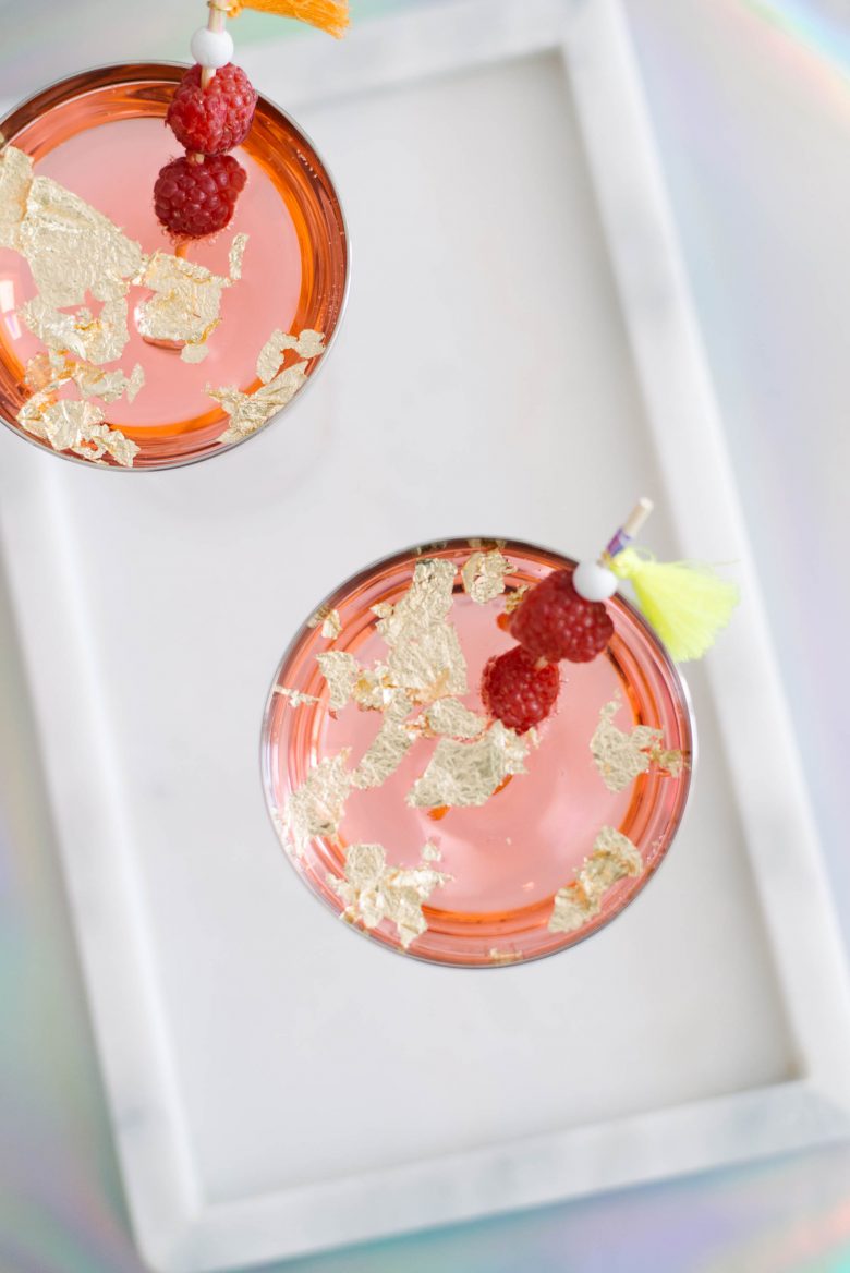 pink cocktails from above with raspberries on swizzle sticks with tassels, with gold leaf