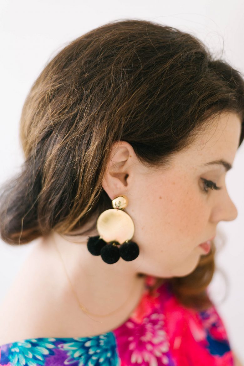 side portrait of woman wearing circular gold earrings with black poms