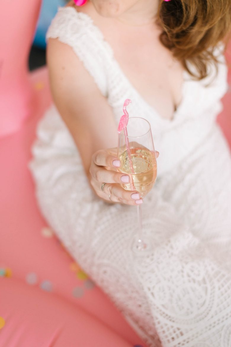 Woman in white holding champagne flute with pink flamingo swizzle stick