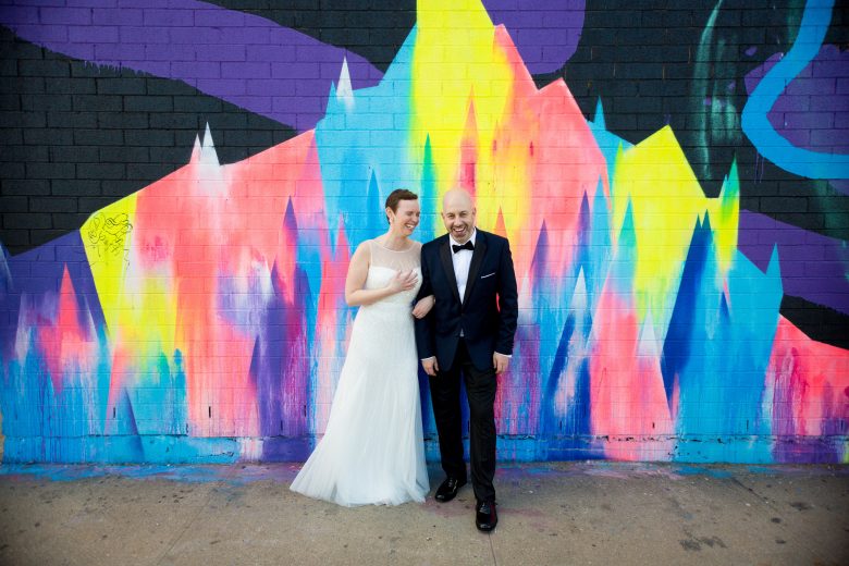 bride and groom in front of colorful graffitied brick wall