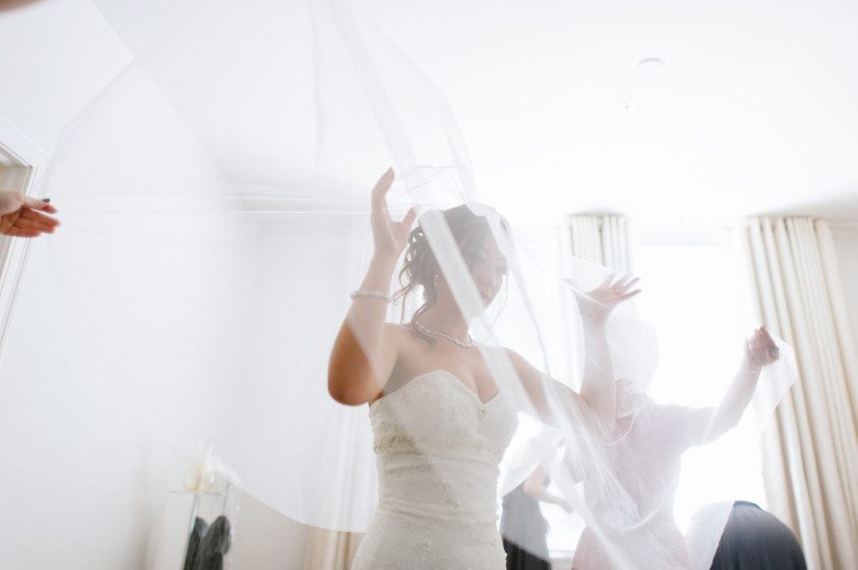 bride in strapless gown being covered with floating veil while getting ready