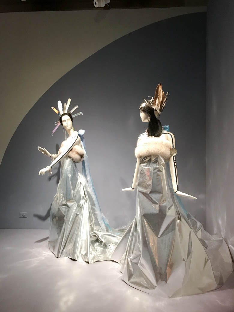 Artwork from the museum of the american indian: mannequins in silver gowns with fur tops, wearing feather headdresses 
