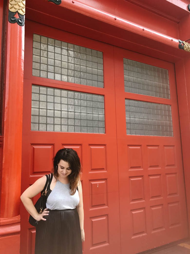 author in grey top and black skirt standing in front of giant red doors