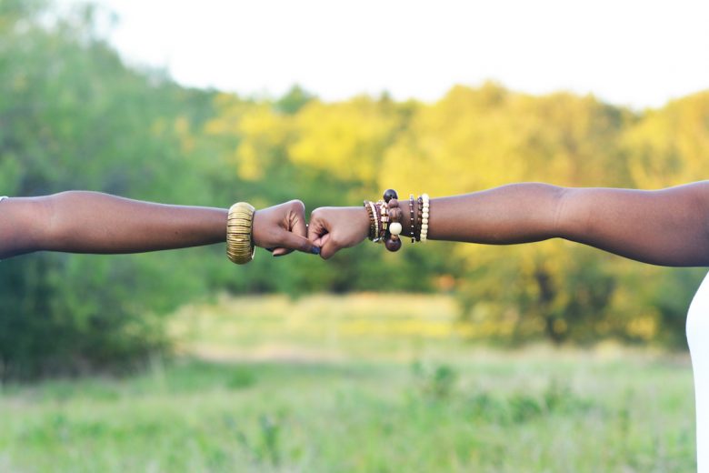 Two hands fist bumping in a field, wearing bracelets
