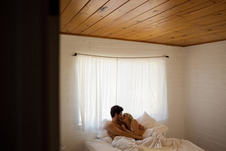 couple in bed with white sheets in front of window