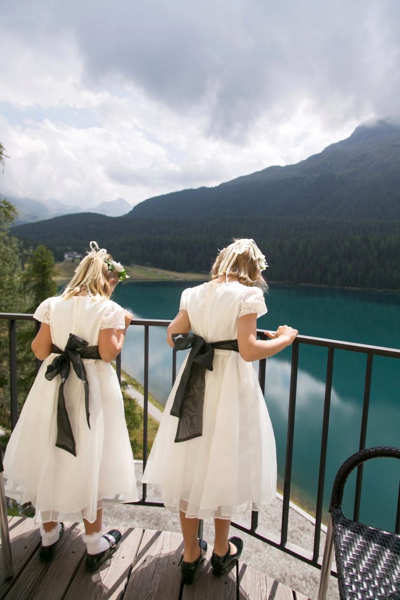 flower girls from behind, looking over balcony railing at blue water and a green mountain