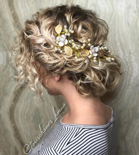 blond curly hair gathered low at the nape of her neck, with gold leaf, pearl, and white enameled flower hair accessory for a wedding hairstyle