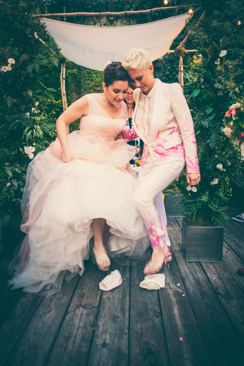 Two women stepping on separate glasses at the end of their wedding ceremony