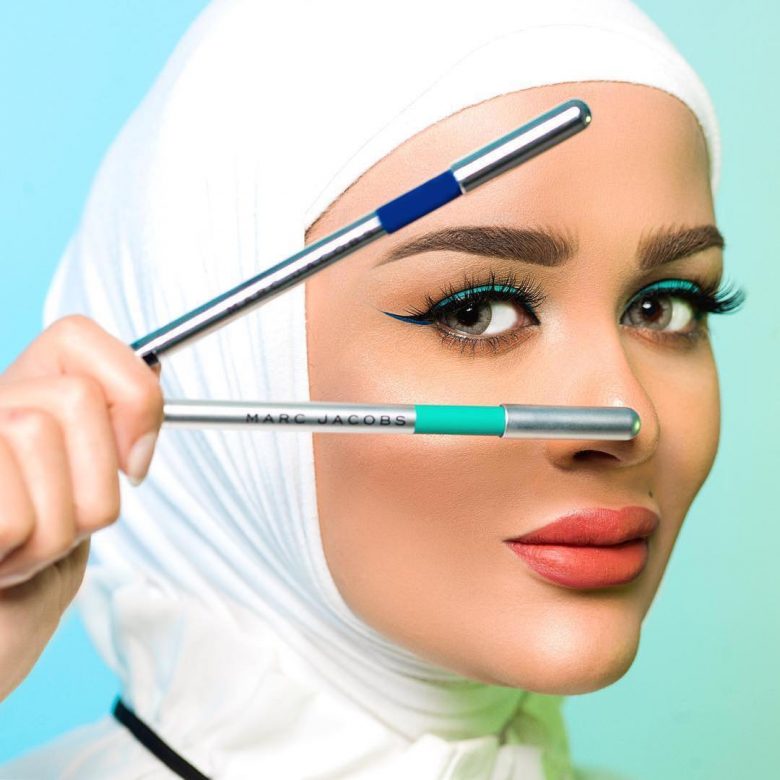 A woman holds two makeup pens looking through them 