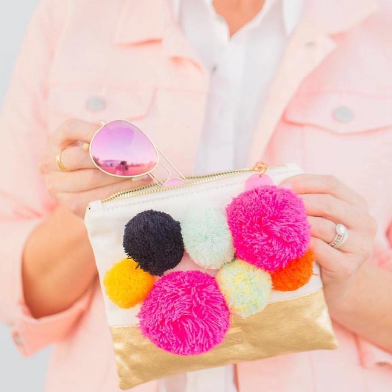 brightly colored poms on a small zipper bag with pink lensed aviators