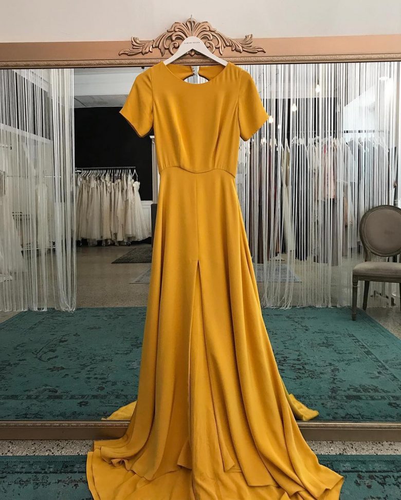marigold gown hanging on a mirror with dark teal carpet in dress boutique