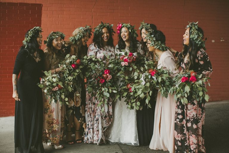 A bridal party stands lined up and laughing while wearing green leafy crowns and giant leafy bouquets