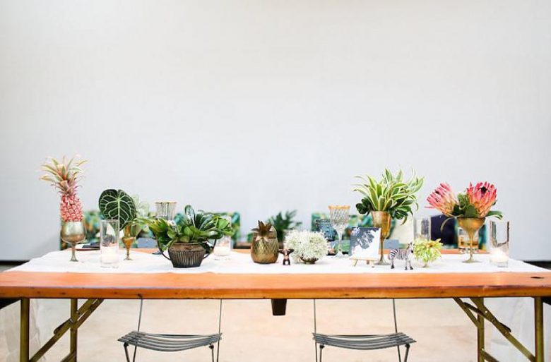 tablescape with tropical-looking plants and flowers in various metallic containers, with small zebra