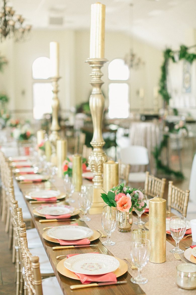 gold and peachy pink tablescape with gold chargers, pink napkins, small pink and green arrangements with gold pillar candles