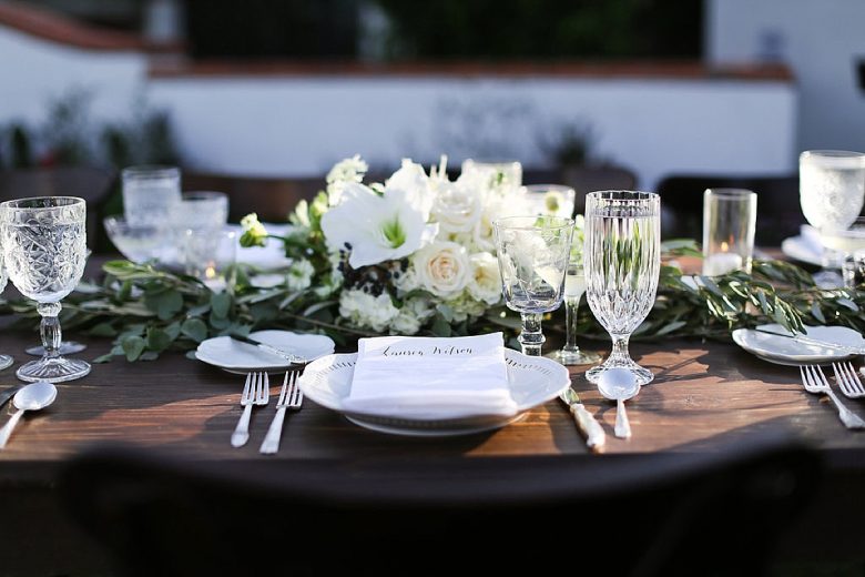 minimal tablescape with white flowers and greenery, white scalloped plates, crystal goblets, silver utensils