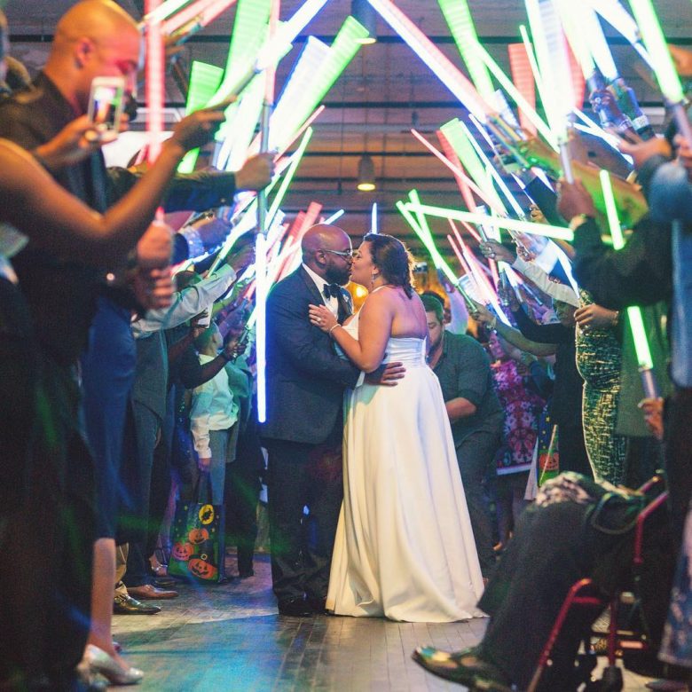 bride and groom kissing while surrounded by guests holding lightsabers to create an arch over them