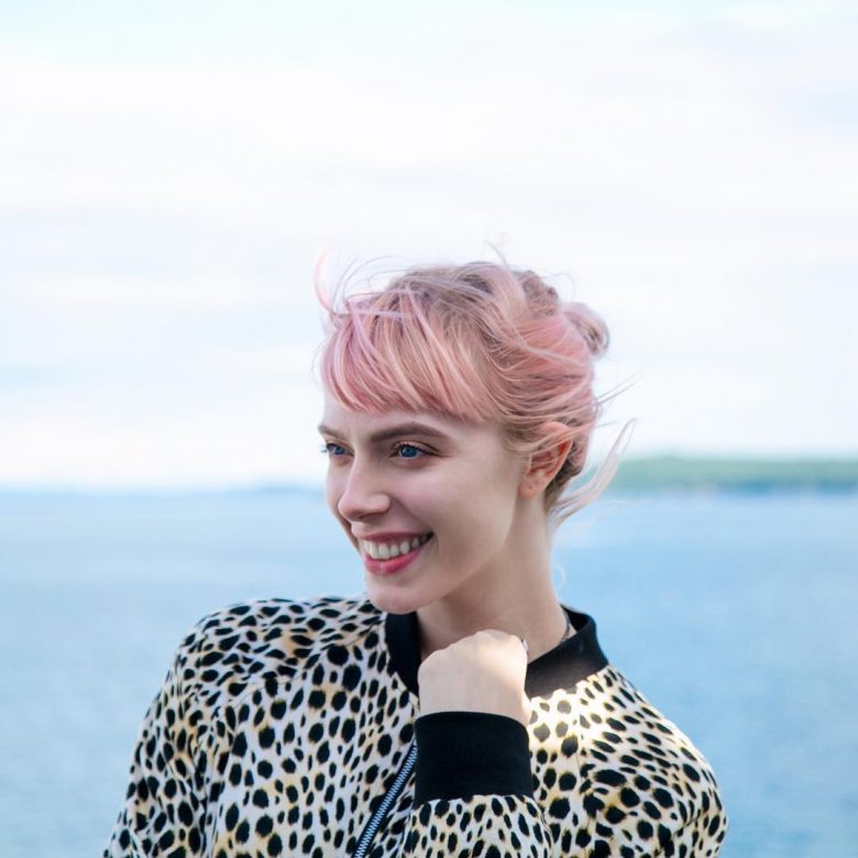 A woman with pink hair wearing a leopard print jacket smiles to the left of frame