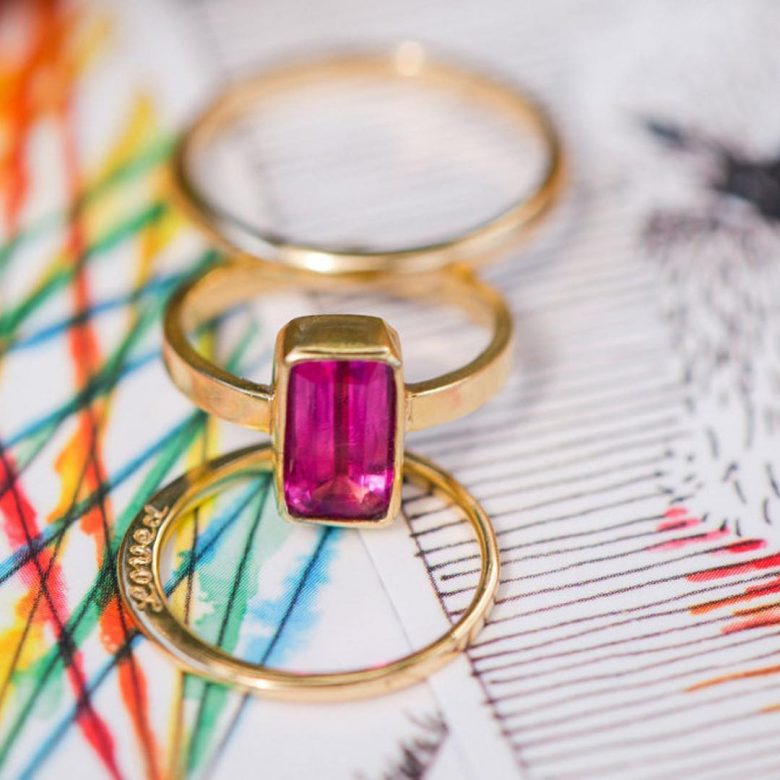 pink emerald cut jewel set in gold band with two other gold bands, one says loved