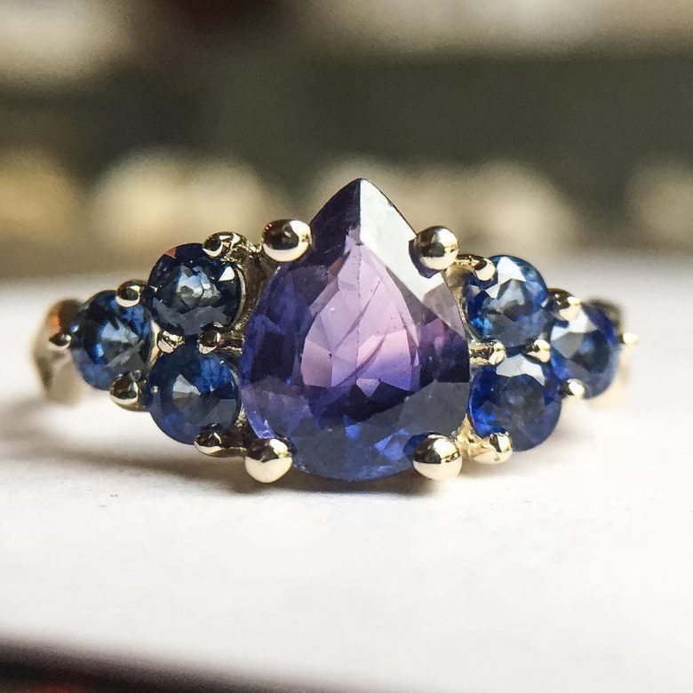 purple teardrop with smaller blue round gems set in yellow gold