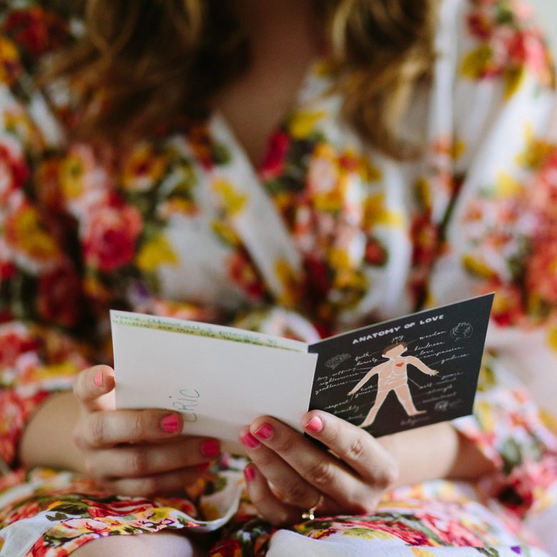 woman in a floral print robe, sitting, and reading a card