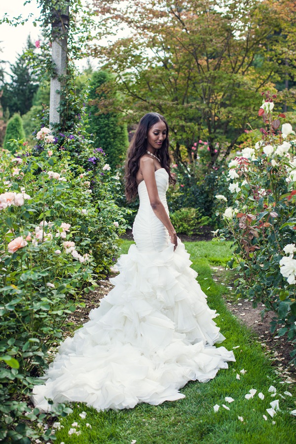 woman in rose garden with long cascading strapless white wedding dress with long dark, wavy hair parted down middle