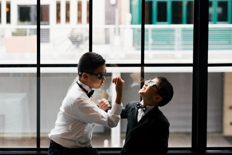 Two young boys in boy ties and glasses playing around in front of warehouse style window