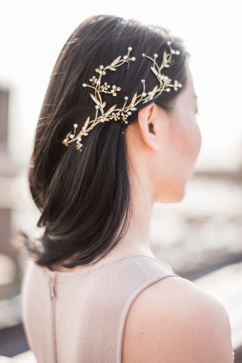 woman with sleek dark shoulder-length hair with the right side secured with a gold and pearl leaf and flower headpiece