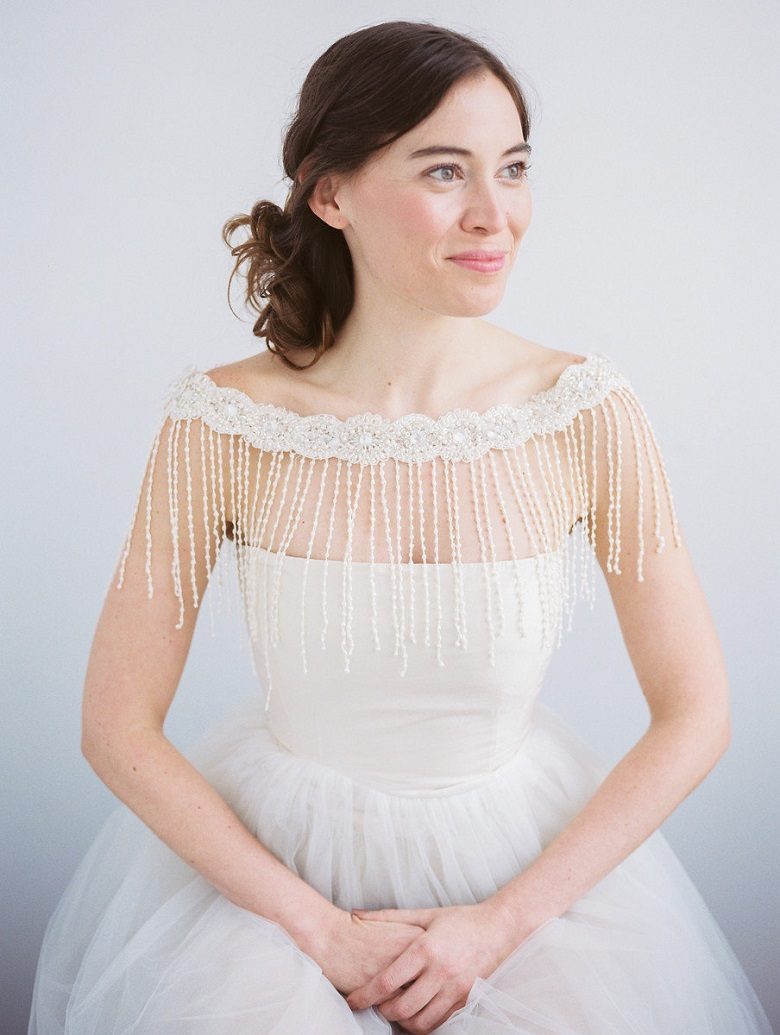 A bride sits and smiles as her fringed bolero hangs from her shoulders