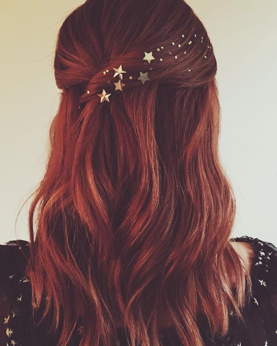 Woman with medium-length dark red loose waves, gently pulled back into a half up style with twist, with gold stars and dots along the twist