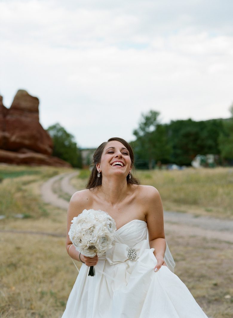 Bride in strapless dress, holding bouquet, with her head back, laughing, near dirt road