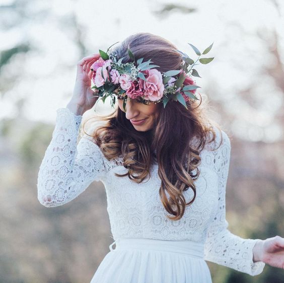 woman in white crochet lace–top wedding dress with long brown soft curls and a large pink and green flower crown