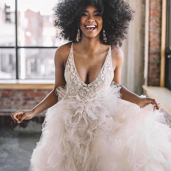 woman wearing lace top, tulle bottom wedding dress, looking delighted, with tightly coiled textured hair 