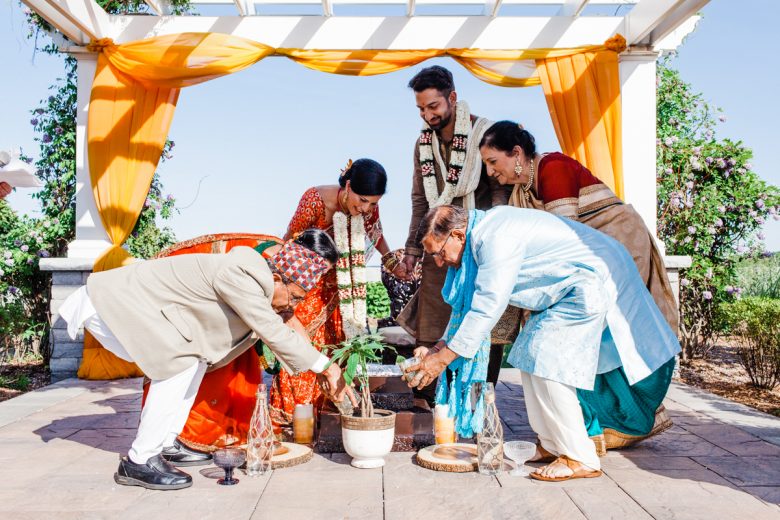 Family members planting and watering tree in small pot with bride and groom