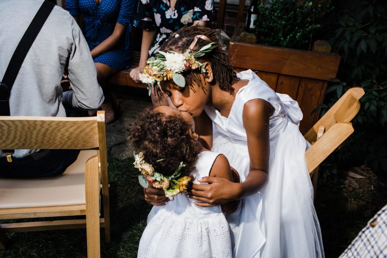 Two flower girls in white dresses with flower crowns kissing