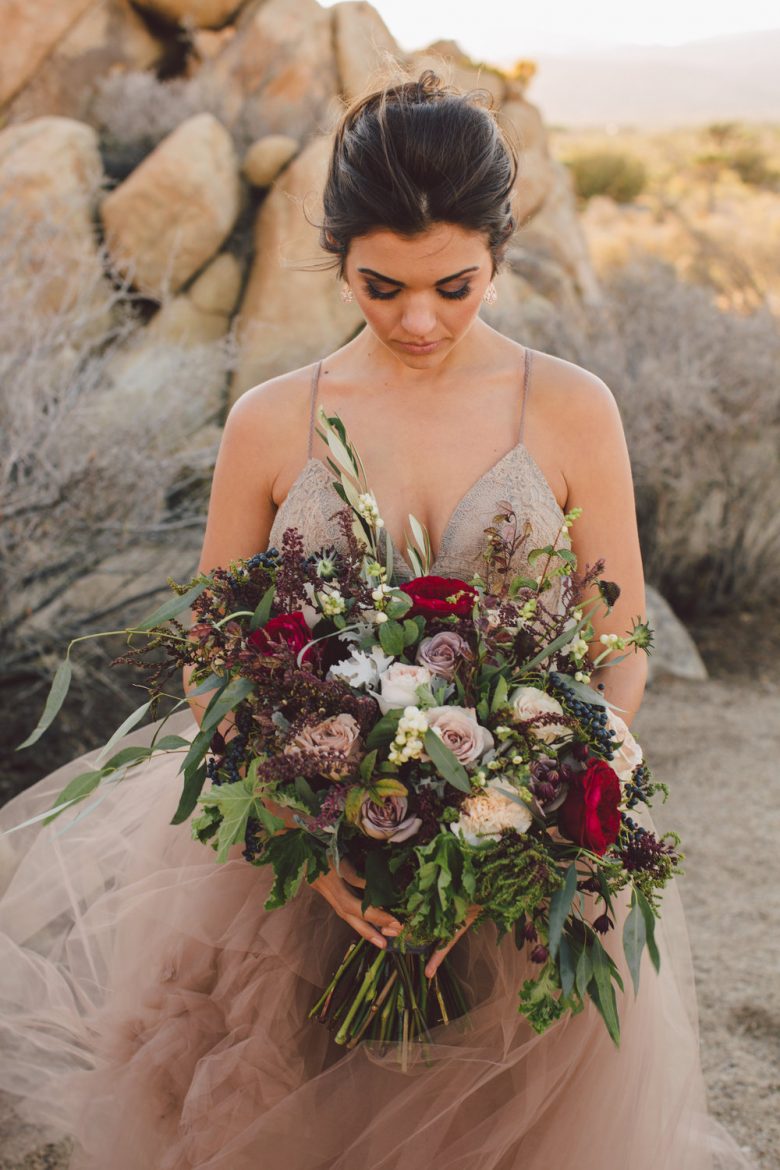 a bride stands amongst boulders as she looks downward towards her bouquet of flowers